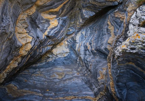 Rock formation in shades of blue and orange with a lot of texture and folded overlapping layers.