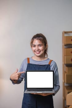 Asian SME business woman showing laptop empty screen at home office. Portrait young Asian small business owner home office, online sell marketing delivery..