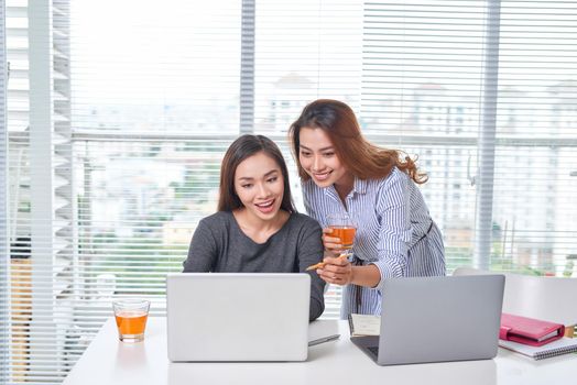 Indoor portrait of smiling girls working together in office. Pretty woman spending time with friend during break and posing for photo in library.