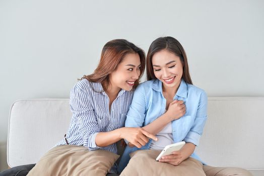 Close up portrait of two excited girlfriends with mobile phones, laughing. Happy joyful female friends resting at home, enjoying talks, having fun.