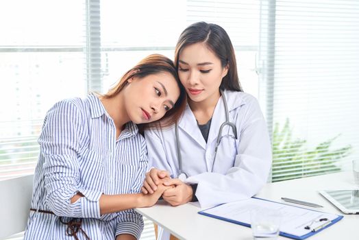 Female doctor talks to female patient in hospital office while writing on the patients health record on the table. Healthcare and medical service. 