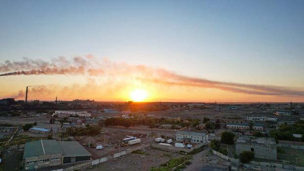 An epic sunset with a view of the smoke of the factory. There are garages and small houses. Near the beach of Lake Balkhash. There are many swifts and different birds flying. Ecology. Air pollution