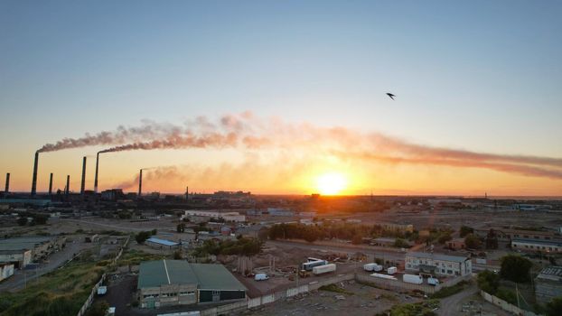 An epic sunset with a view of the smoke of the factory. There are garages and small houses. Near the beach of Lake Balkhash. There are many swifts and different birds flying. Ecology. Air pollution