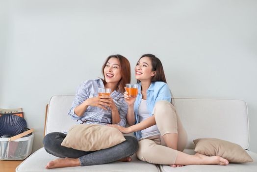 Two friends talking and enjoying a orange juice sitting on a couch in the living room at home