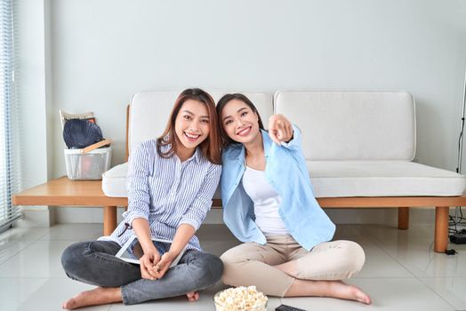 Wondered amazed impressed girl gesturing forefinger eating popcorn watching funny comic program with her friend sitting in living room indoor enjoying interesting film