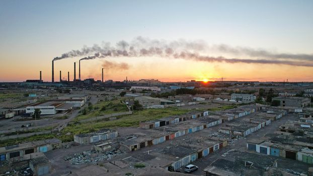 An epic sunset with a view of the smoking factory and the city. The embankment of Lake Balkhash. Low houses are standing and there are few trees. The pipes from the factory are smoking. Kazakhstan