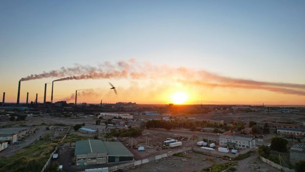 An epic sunset with a view of the smoke of the factory. There are garages and small houses. Near the beach of Lake Balkhash. There are many swifts and different birds flying. Ecology. Air pollution