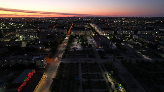 The outskirts of the city. There are old houses, garages and fences. In the distance, you can see the TV tower and the city. Swifts fly. The sky is shimmering purple-blue. Shooting from a drone.