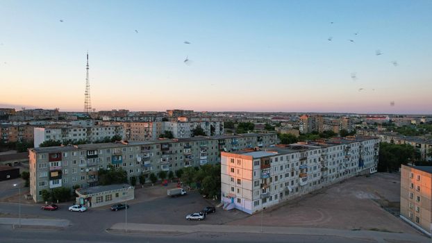 The outskirts of the city. There are old houses, garages and fences. In the distance, you can see the TV tower and the city. Swifts fly. The sky is shimmering purple-blue. Shooting from a drone.