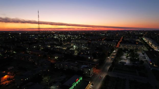 The outskirts of the city. There are old houses, garages and fences. In the distance, you can see the TV tower and the city. Swifts fly. The sky is shimmering purple-blue. Shooting from a drone.