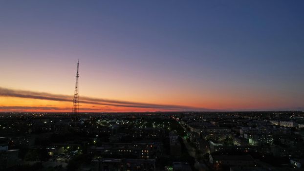 The outskirts of the city. There are old houses, garages and fences. In the distance, you can see the TV tower and the city. Swifts fly. The sky is shimmering purple-blue. Shooting from a drone.