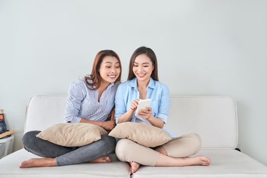 Close up portrait of two excited girlfriends with mobile phones, laughing. Happy joyful female friends resting at home, enjoying talks, having fun.