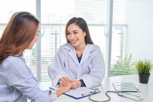 Female doctor talks to female patient in hospital office while writing on the patients health record on the table. Healthcare and medical service. 