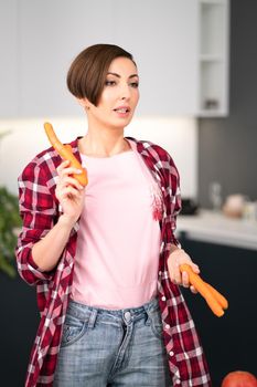 Charming short hair housewife with fresh carrot in the hands prepares carrot cake in the kitchen. Healthy food at home. Healthy food leaving concept. 