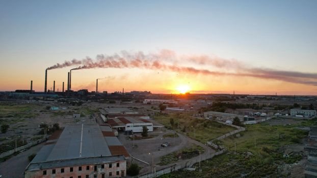 An epic sunset with a view of the smoking factory and the city. The embankment of Lake Balkhash. Low houses are standing and there are few trees. The pipes from the factory are smoking. Kazakhstan