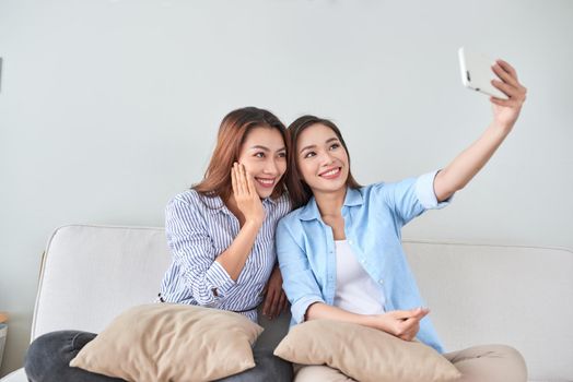 Close up portrait of two excited girlfriends with mobile phones, laughing. Happy joyful female friends resting at home, enjoying talks, having fun.