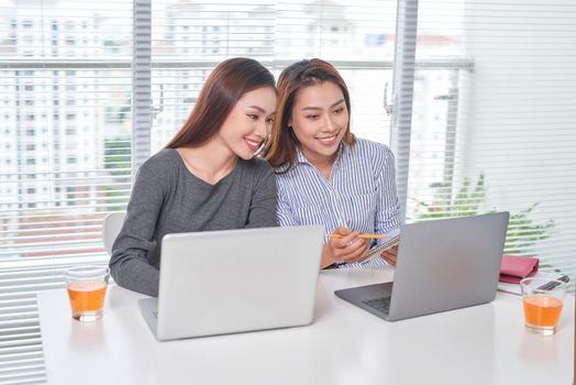 Indoor portrait of smiling girls working together in office. Pretty woman spending time with friend during break and posing for photo in library.