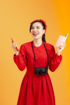 Travel concept. Young happy female Asian tourist holding passport with flight tickets, isolated on orange background