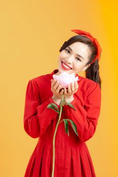 Portrait of an attractive young Asian woman in red dress holding peony flower isolated over orange background