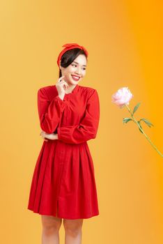 Young Asian woman happy to receive peony rose when standing isolated on orange background.