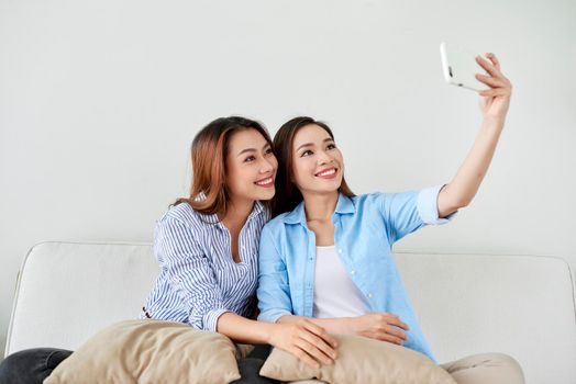 Close up portrait of two excited girlfriends with mobile phones, laughing. Happy joyful female friends resting at home, enjoying talks, having fun.