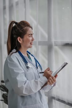 Medical health clinic beautiful Asian doctor working using laptop stethoscope diagnosing patient analysis. ..Female Asian doctor looking outside holding a tablet....