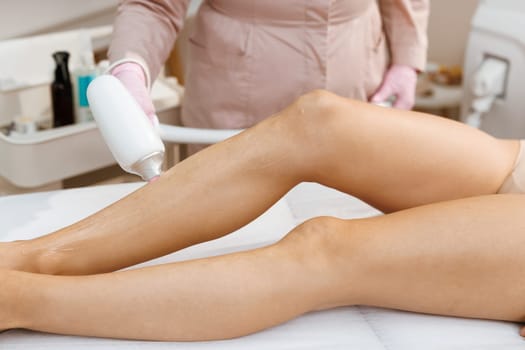 Professional beautician or cosmetologist use special ointment and apparatus. Soft and smooth hairless skin on legs. Close-up woman's perfect legs while getting hair removal procedure in salon.