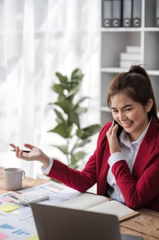 Asian businesswoman in formal suit in office happy and cheerful during using smartphone and working..