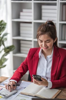 Asian businesswoman in formal suit in office happy and cheerful during using smartphone and working..