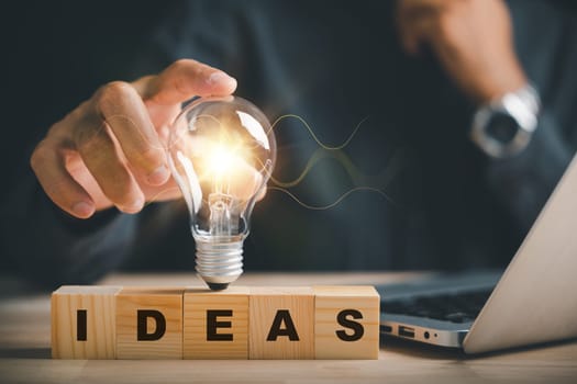 New idea concept A man hand holds light bulb while word Ideas sits on wooden block. Showcases power of innovation, inspiration, and business startups. Symbolizes ability to think creatively.