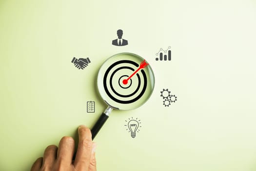 The image showcases a businessman using a magnifying glass to zoom in on the target goal icon, symbolizing the essential strategies for success in business and sustainable goals.