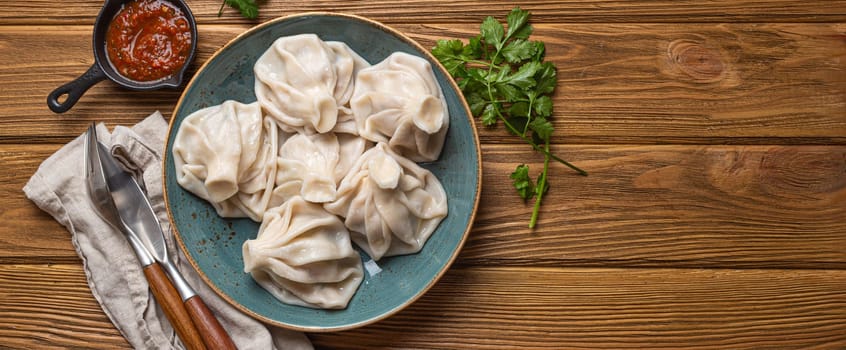 Georgian dumplings Khinkali on plate with red tomato sauce and fresh cilantro top view on rustic wooden background, traditional dish of Georgia, space for text