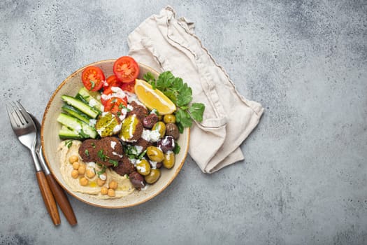 Falafel salad bowl with hummus, vegetables, olives, herbs and yogurt sauce. Vegan lunch plate top view on rustic stone background, healthy meal with falafel and veggies, space for text