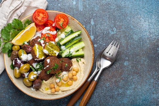Falafel salad bowl with hummus, vegetables, olives, herbs and yogurt sauce. Vegan lunch plate top view on rustic stone background, healthy meal with falafel and veggies, space for text