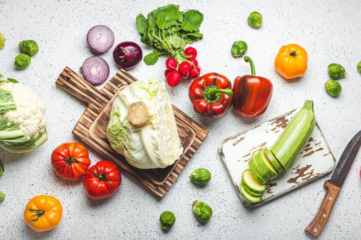 Fresh various vegetables with wooden cutting boards and knife on white kitchen table top view. Cooking vegetarian meal from healthy ingredients, diet food and nutrition concept