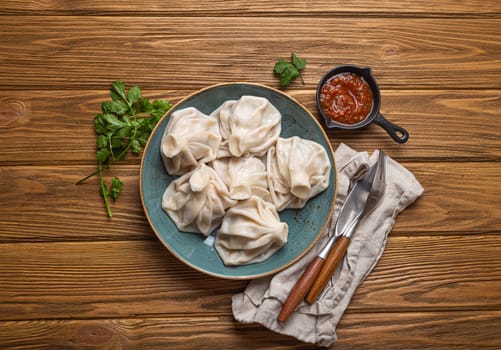 Georgian dumplings Khinkali on plate with red tomato sauce and fresh cilantro top view on rustic wooden background, traditional dish of Georgia
