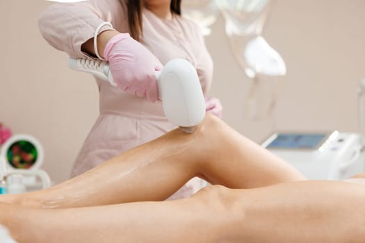 Hair removal on the legs, laser procedure at clinic. Beautician removes hair on beautiful female legs using a laser. Midsection of female beautician using laser machine on customer's leg at salon