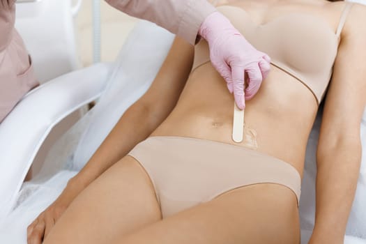 Woman wearing protective gloves applying gel on woman's bikini area to prepare for laser depilation. Bikini laser epilation and cosmetology. Hair removal cosmetology procedure.