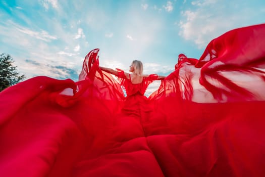 Woman Red Flying Dress. A blonde in a red dress against the sky. Rear view of a beautiful blonde woman in a red dress fluttering in the wind against a blue sky and clouds
