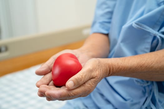 Asian elderly woman patient holding red heart in her hand on bed in hospital, healthy strong medical concept.