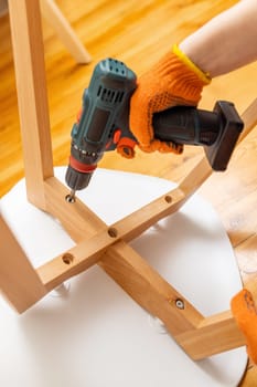 Craftsman collecting and repairing with tools, assembling furniture with drill. Man screws details to chair with electric screwdriver at home after renovation