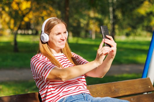 A woman wearing headphones listening to music, breathing fresh air, relaxing while sitting on a bench in sunny day in the park