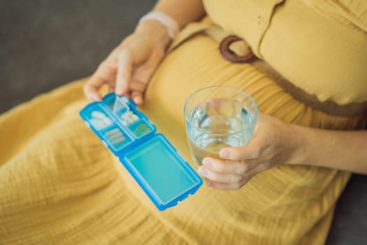 Prenatal Vitamins. Portrait Of Beautiful Smiling Pregnant Woman Holding Pill Box and a glass of water, Taking Supplements For Healthy Pregnancy While Sitting On Couch At Home, Free Space.