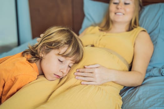 Young pregnant mother hugging her little boy lying in bed at night. Caring and loving parent hugging child.