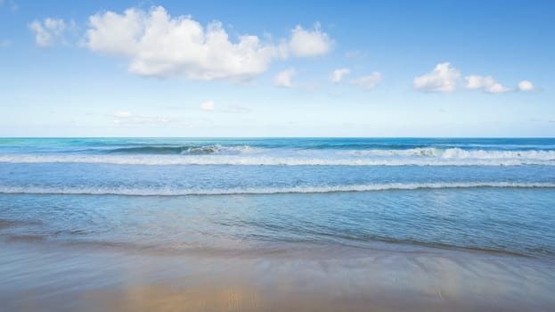 Golden sand and blue ocean water with white clouds. Karon Beach. In places, high waves and splashes. Blue sky. The sun's rays are reflected on the sand. White foam from the waves. Thailand