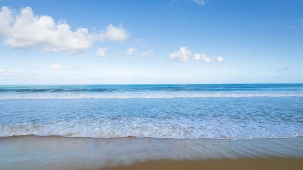 Golden sand and blue ocean water with white clouds. Karon Beach. In places, high waves and splashes. Blue sky. The sun's rays are reflected on the sand. White foam from the waves. Thailand