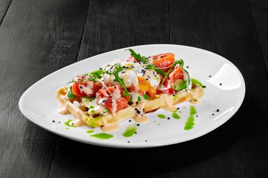 Delicious Belgian waffle topped with avocado slices, salty salmon fillet, poached egg and fresh arugula dressed with sauce. Mediterranean style brunch
