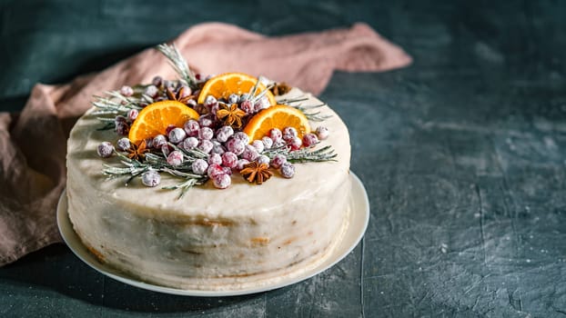 Winter homemade cake on dark background. White cream christmas cake decored rosemary, cranberries, star anise and oranges slices. Copy space