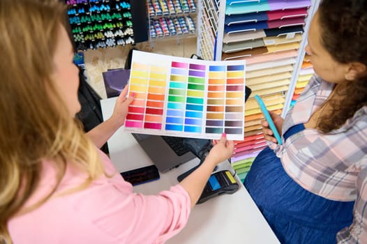 Selective focus on a palette with color swatches of watercolor paints of various spectrums, in the hands of a saleswoman demonstrating it to customer shopping in a stationery store. Painting and art