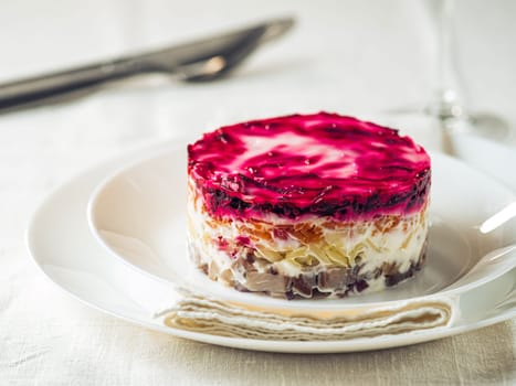 Layered salad herring under fur coat on table. Portion of traditional russian salad with herring, beet and other vegetables on white linen tablecloth. Copy space
